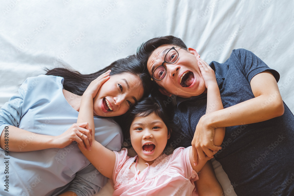 快乐的亚洲家庭躺在卧室的床上，面带微笑，俯视图