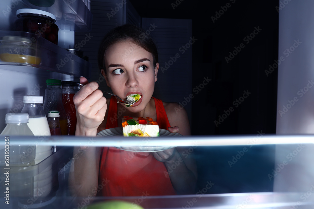 一个在冰箱附近吃东西的年轻女人，从里面看
