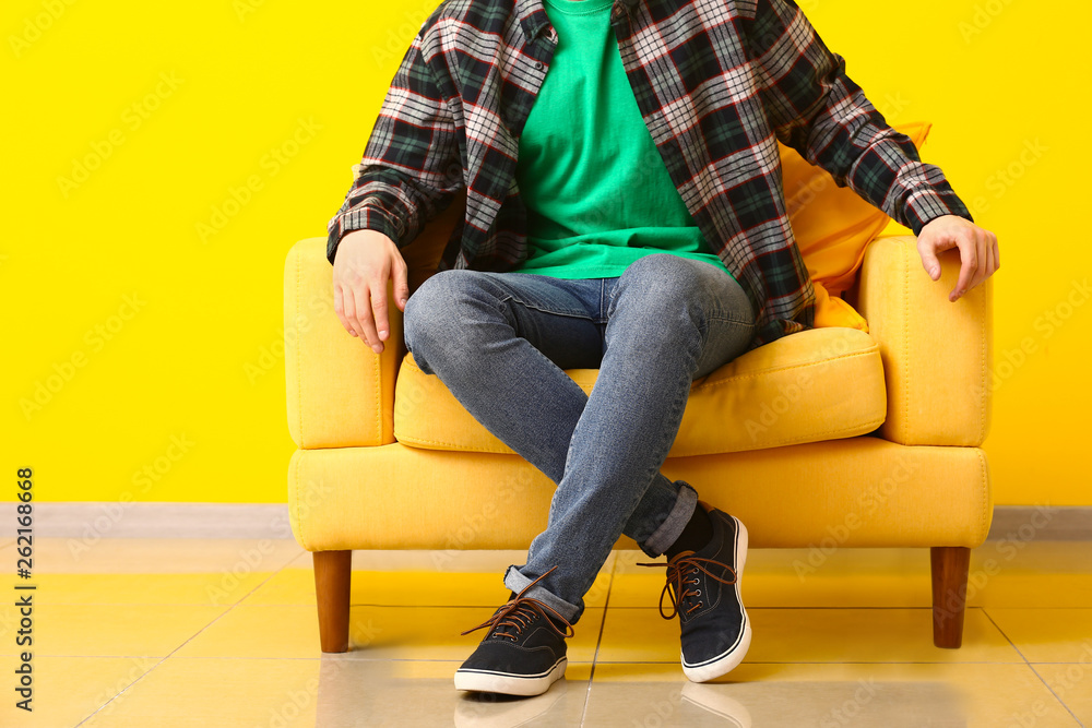 时尚的男人穿着鞋子坐在靠近彩色墙的扶手椅上