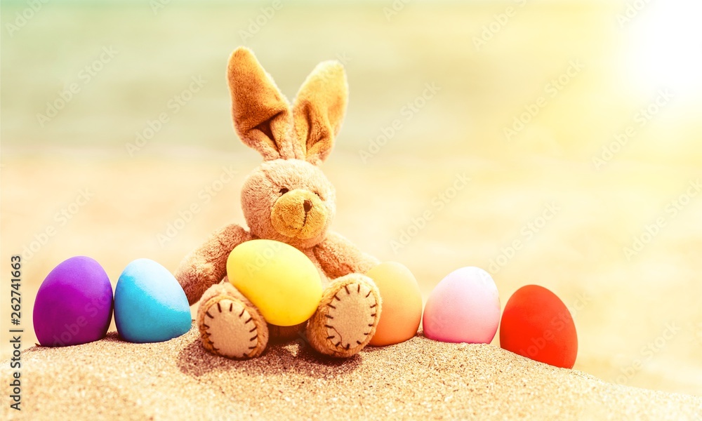Easter bunny and color eggs on the sandy beach by the ocean