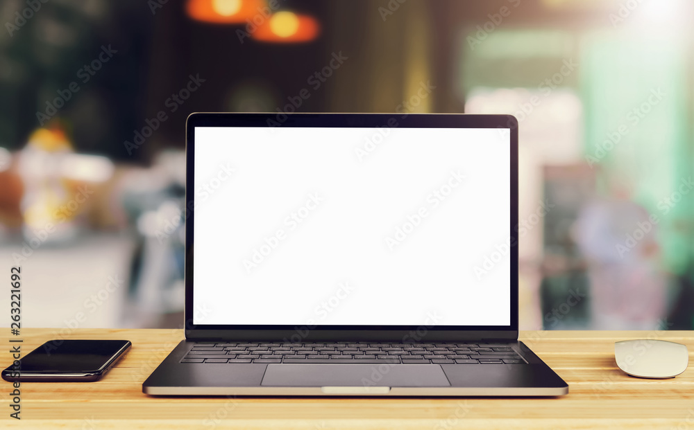 咖啡馆背景下桌上的笔记本电脑空白白色屏幕和手机