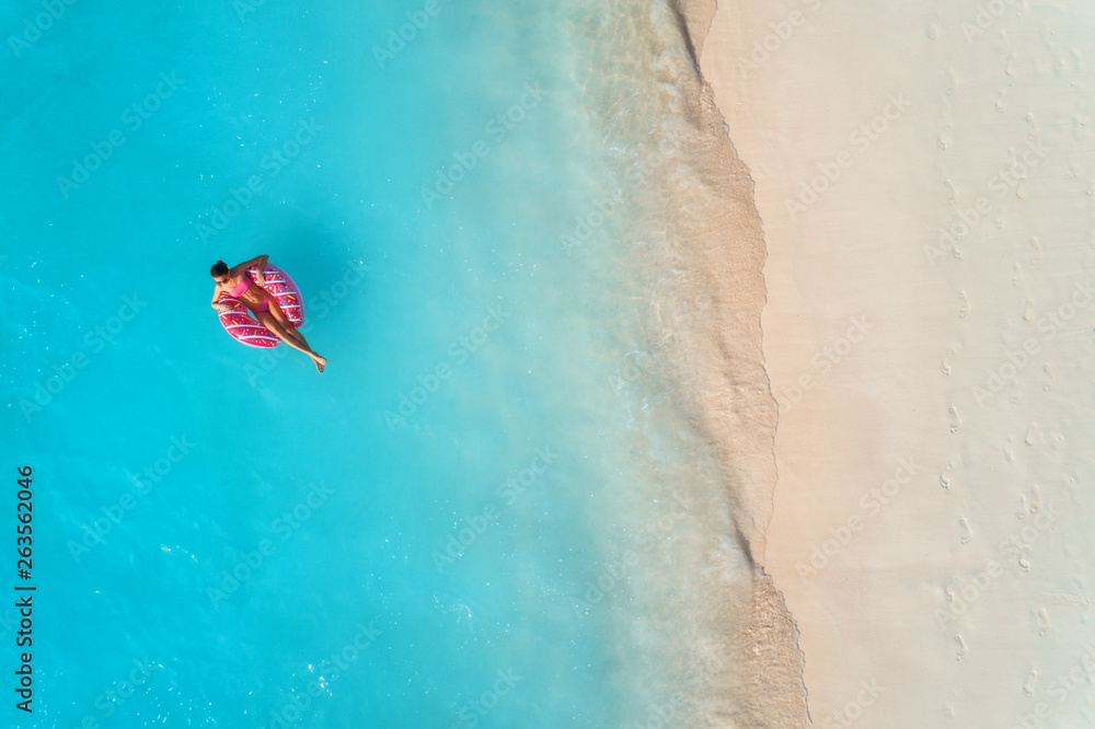 一名年轻女子带着甜甜圈在清澈的蓝色大海中游泳的鸟瞰图，海浪拍打着s