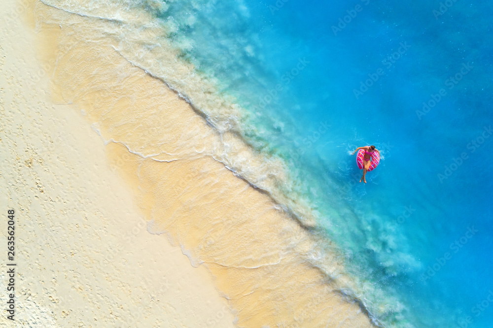 一名年轻女子带着甜甜圈在清澈的蓝色大海中游泳的鸟瞰图，海浪拍打着s