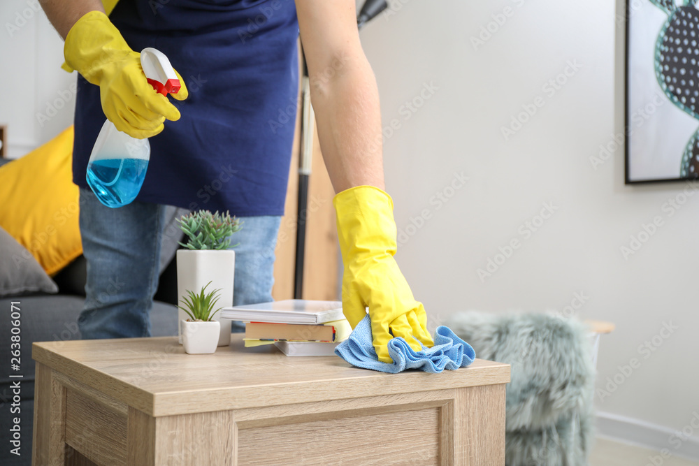 Male janitor cleaning table in room