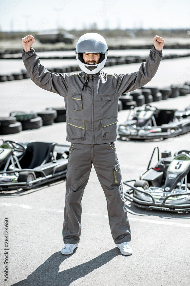 一位身穿防护运动服的快乐赛车手站在卡丁车比赛中获胜的全身肖像
