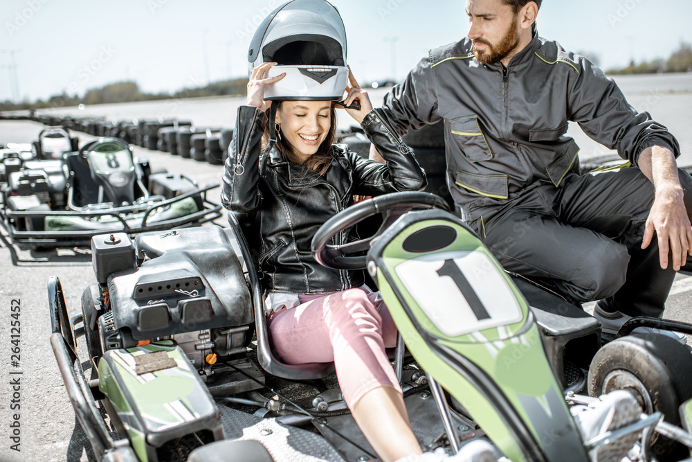Instructor with happy young woman driver wearing protective helmet before the race on the go-kart tr