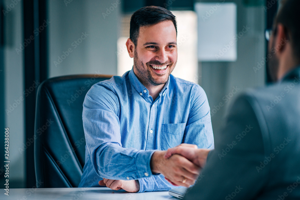 两位面带微笑的商人坐在办公桌前握手。