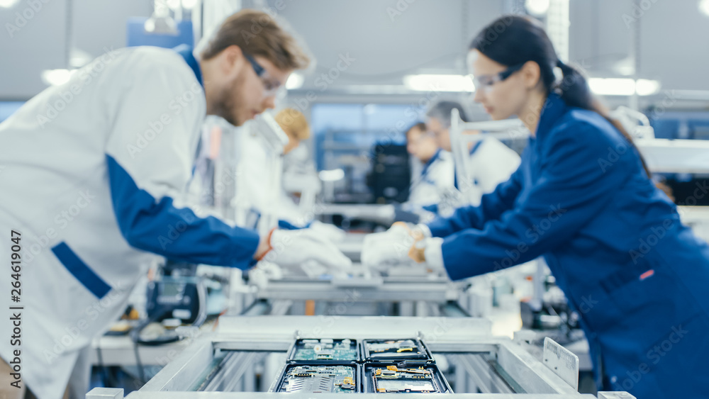 一家电子厂工人站在资产上手工组装电路板的照片