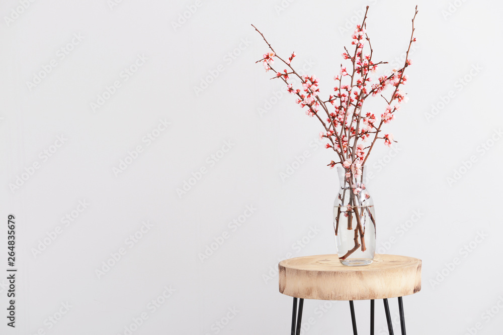 在浅色背景下，桌子上摆放着美丽的开花树枝的花瓶