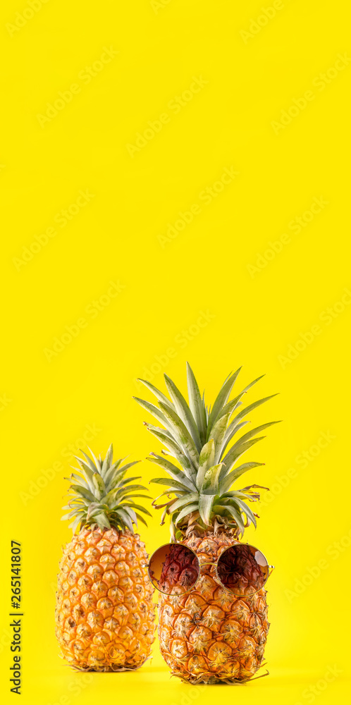Creative pineapple looking up with sunglasses and shell isolated on yellow background, summer vacati