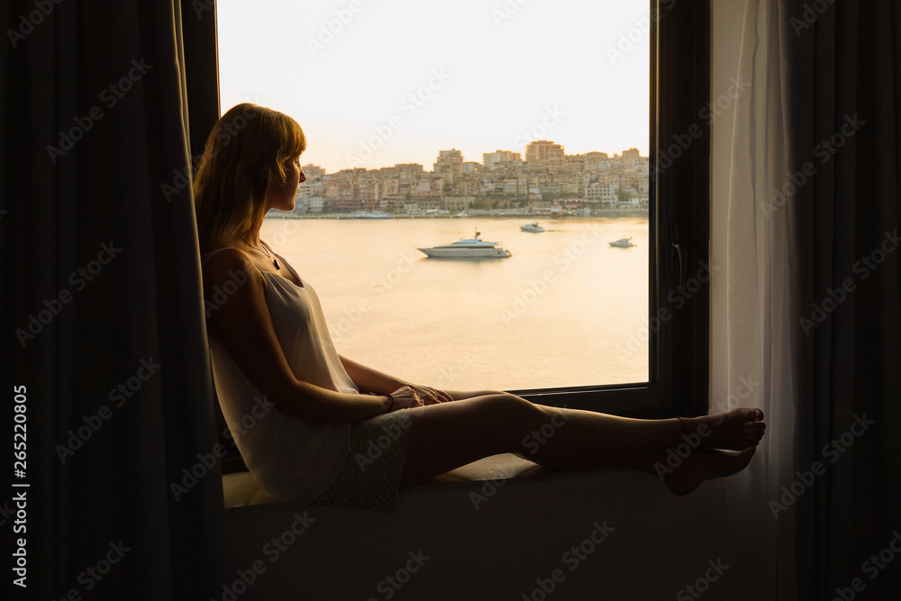 CLOSE UP: Young blonde woman relaxing on window watching sun rising in Albania
