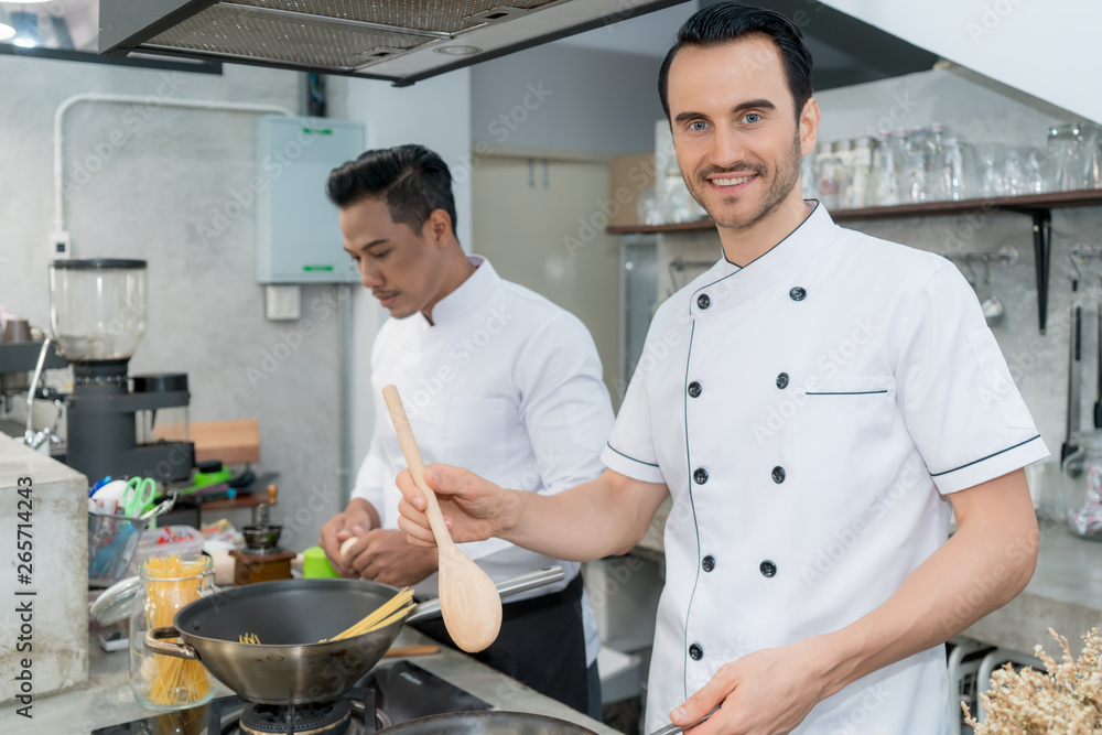 年轻男厨师与同事在厨房准备意大利面的肖像。