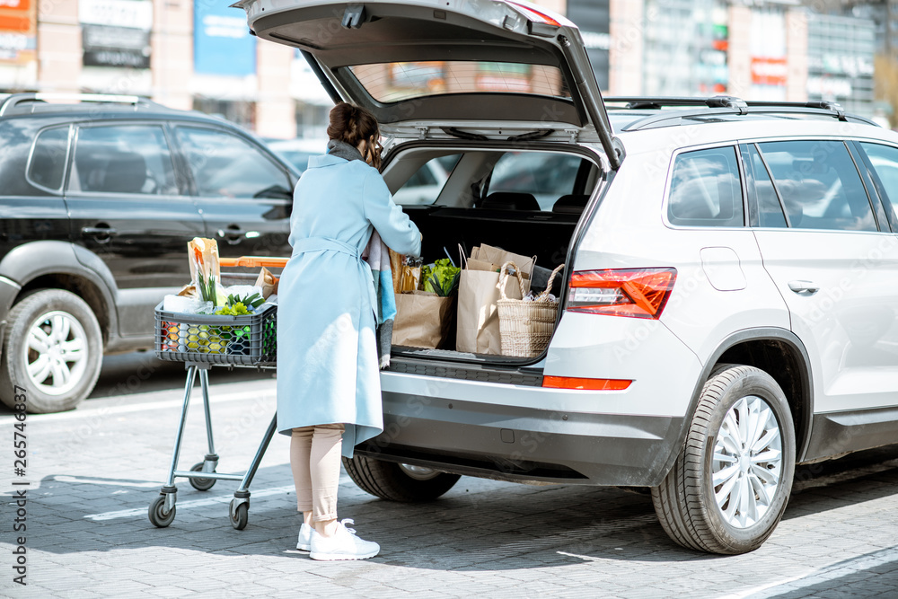 一名妇女将在超市买的食物打包到停车场的汽车行李箱中