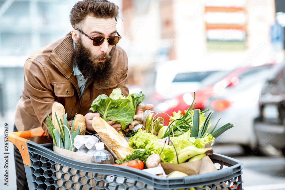 户外停车场上一个时尚男人的画像，他的购物车里装满了新鲜健康的食物