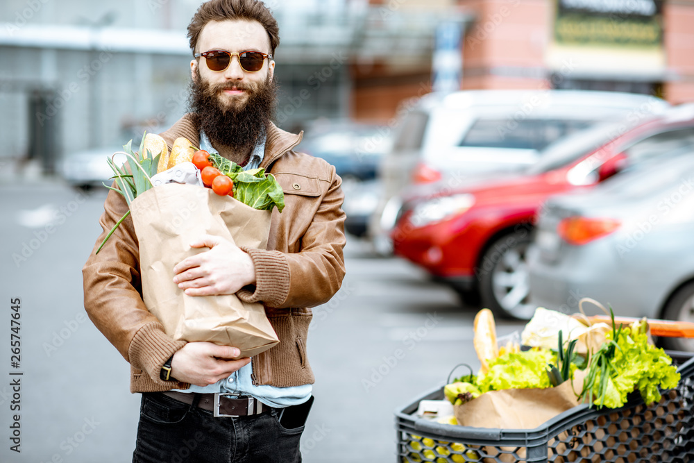 快乐时尚的男人，带着装满新鲜健康食品的购物袋，在超市附近的户外
