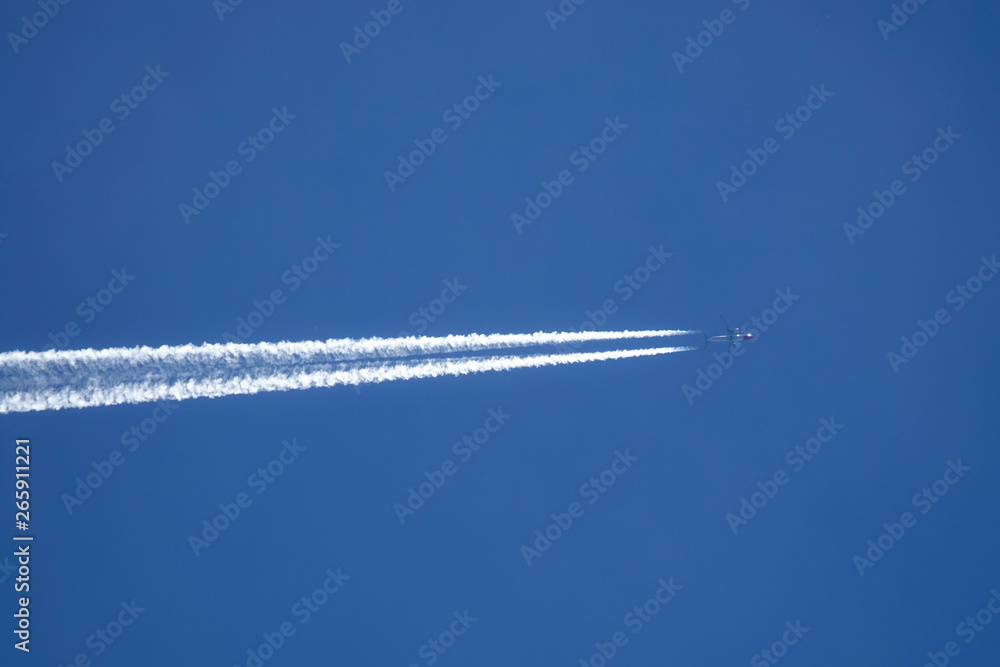 VERTICAL BOTTOM UP: Airplane flies across the sky, leaving a long white trail.