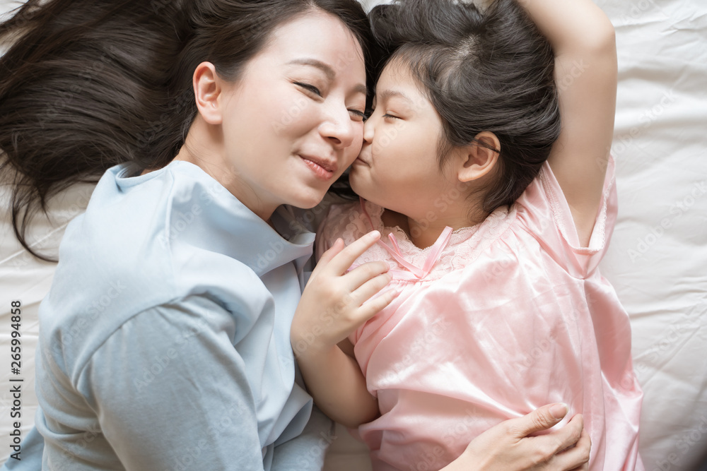 Daughter kisses her mothers cheek. and hugging in the bedroom .Happy Asian family