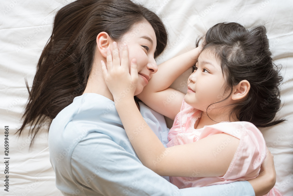 母亲和她的女儿小女孩在卧室里拥抱和抚摸她的妈妈。快乐的亚洲家庭