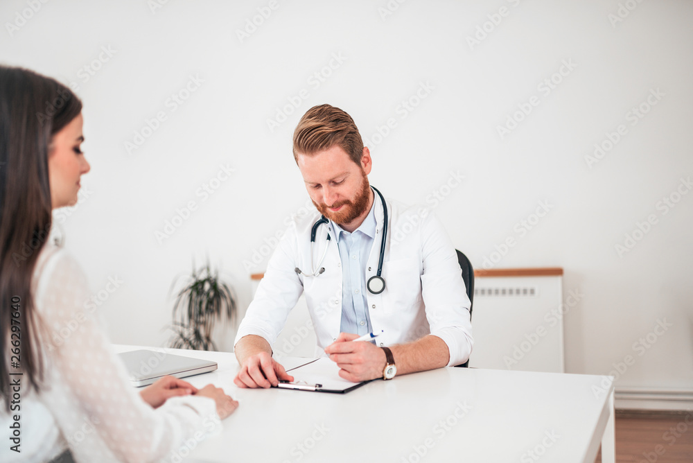 Doctor writing application form while consulting female patient in the office.