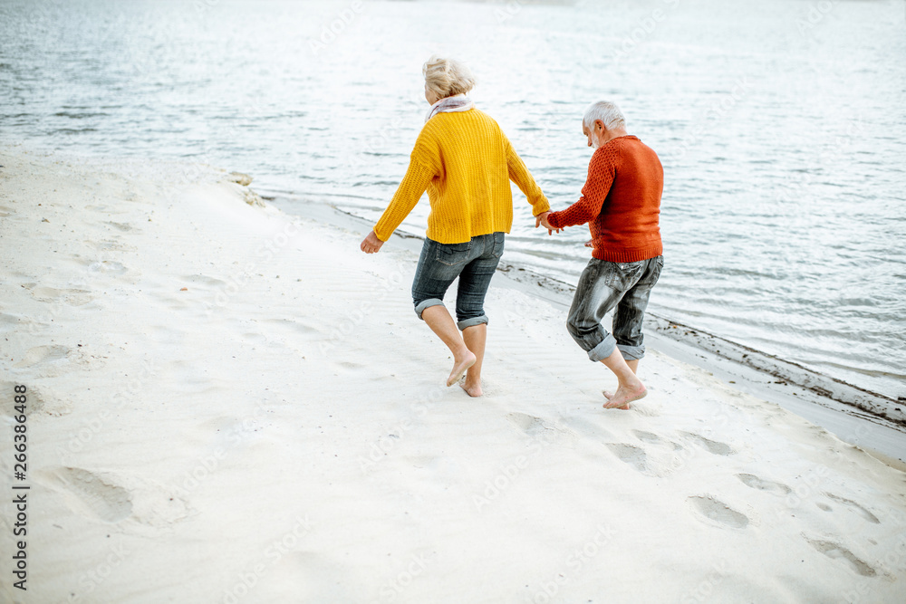 可爱的高级情侣穿着五颜六色的毛衣走在沙滩上，享受空闲时间