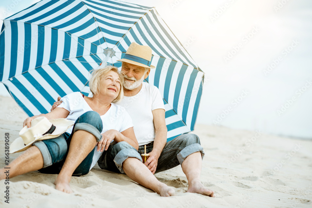 快乐的老年夫妇放松身心，一起躺在沙滩上的雨伞下，享受他们的时光