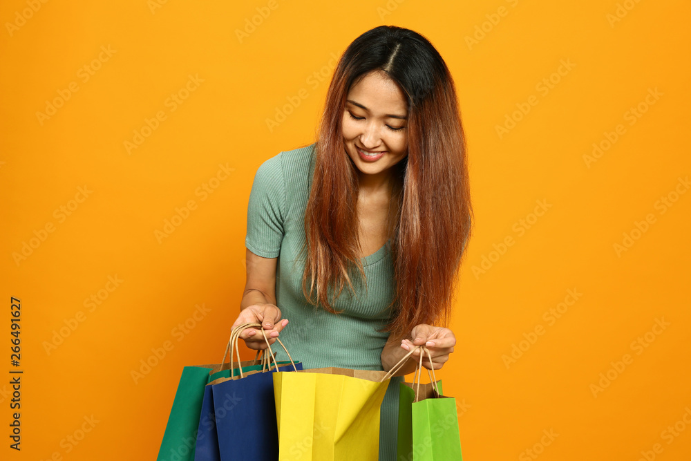 Asian woman with shopping bags on color background
