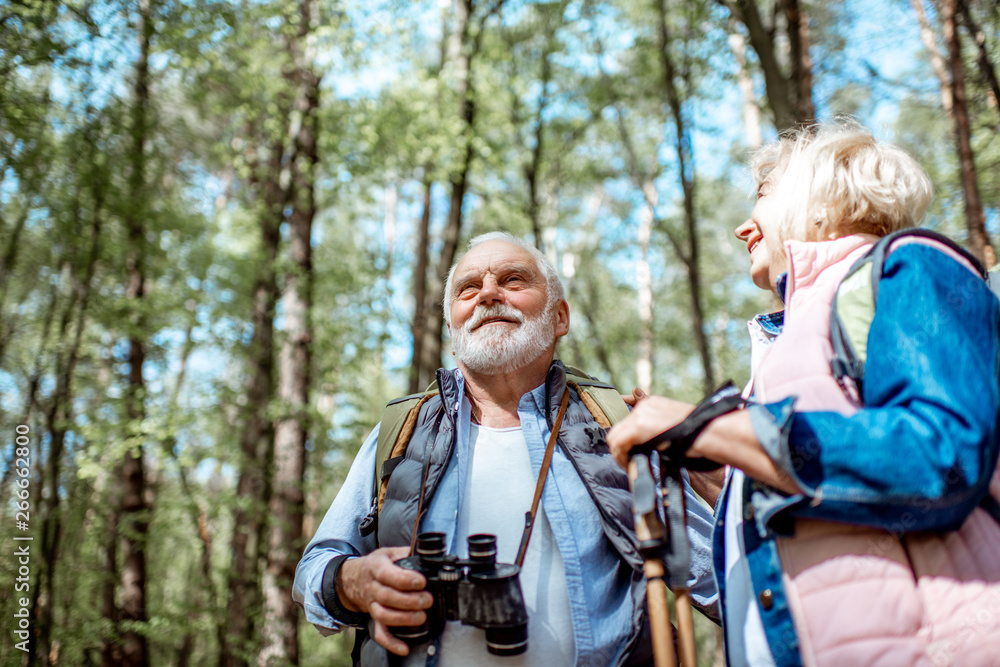 一对老年夫妇在森林里徒步旅行时用双筒望远镜观看。关于积极生活方式的概念