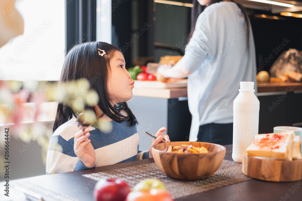 Asian girl kid having breakfast cereal at home kitchen