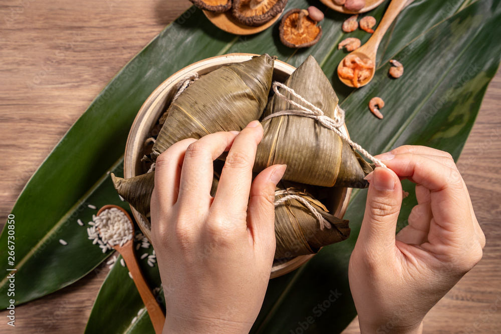 Zongzi, woman eating steamed rice dumplings on wooden table, food in dragon boat festival duanwu con