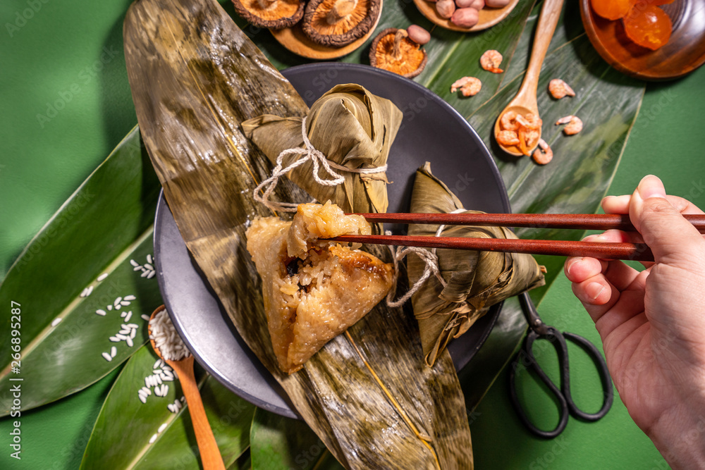 Zongzi, woman eating steamed rice dumplings on green table background, food in dragon boat festival 