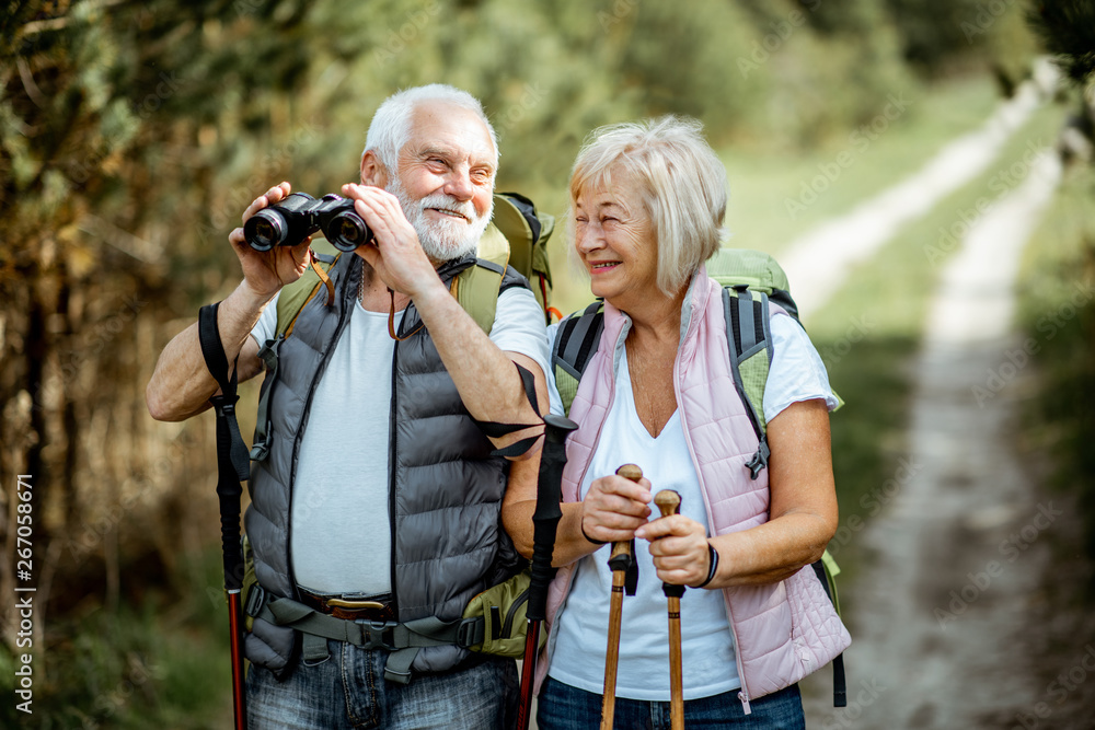 一对幸福的老年夫妇带着双筒望远镜、背包和徒步旅行棒站在一起的肖像w