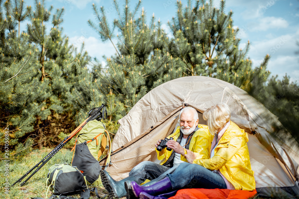一对穿着黄色雨衣的老年夫妇一起坐在树林里露营地的帐篷附近