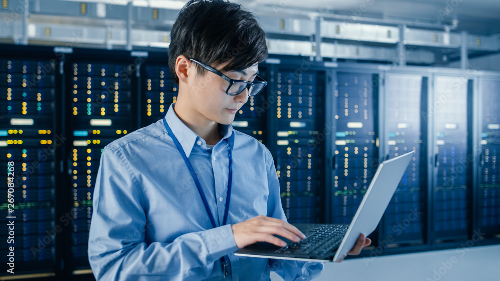 In the Modern Data Center: Portrait of IT Engineer Standing with Server Racks Behind Him, Doing Main