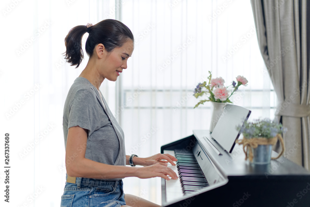 亚洲美女在家弹电子钢琴。按钢琴时的侧视图