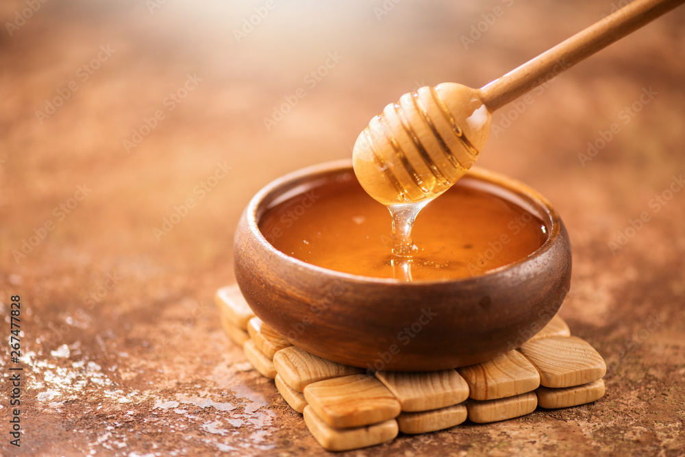 蜂蜜从木碗中的蜂蜜勺中滴下。健康的有机浓蜂蜜从木盆中倒出