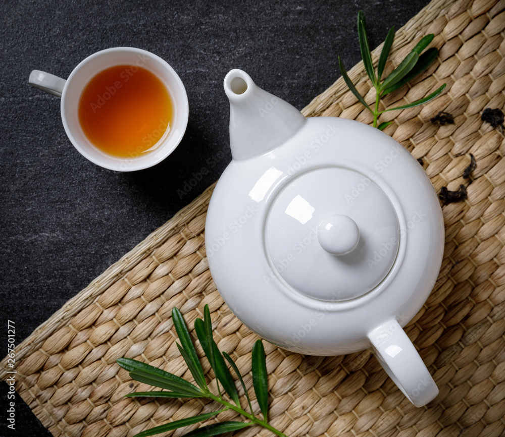 Cup of hot tea with steaming jugs and dry tea on the plate mat on the black stone table background w