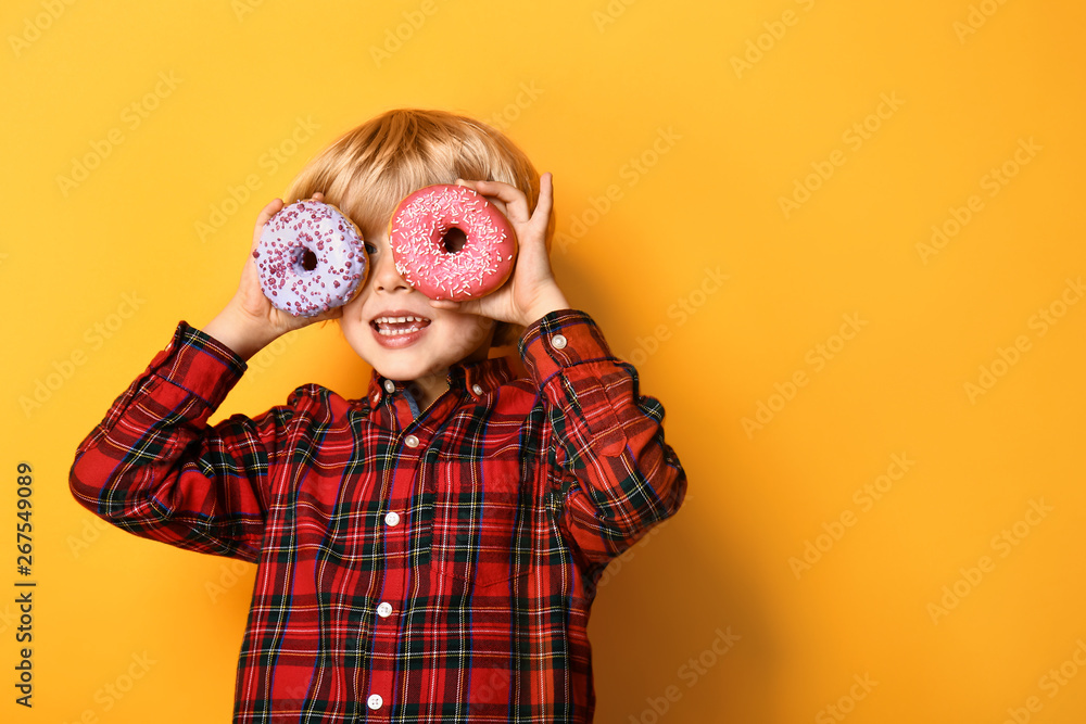 Happy little boy with tasty donuts on color background