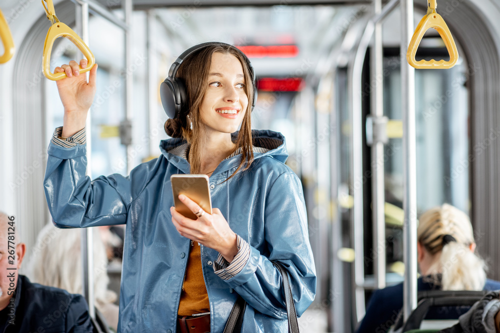 年轻的女乘客戴着耳机和智能手机站在现代有轨电车上，尽情享受
