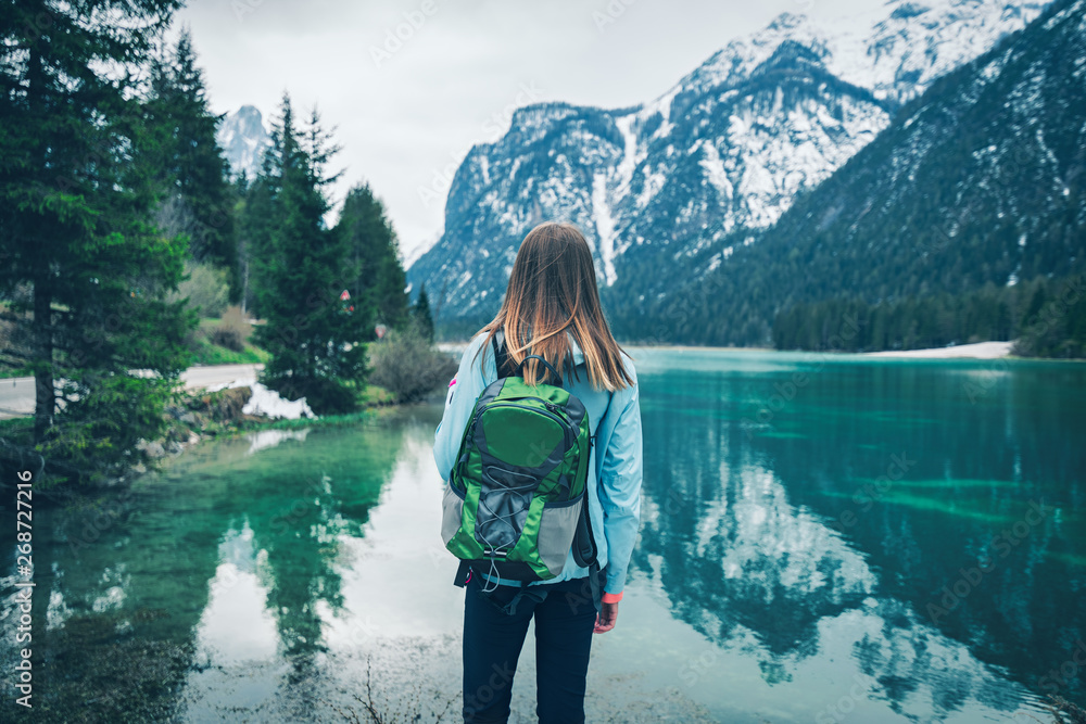 春天阴天，背着绿色背包的年轻女子站在山湖岸边。T
