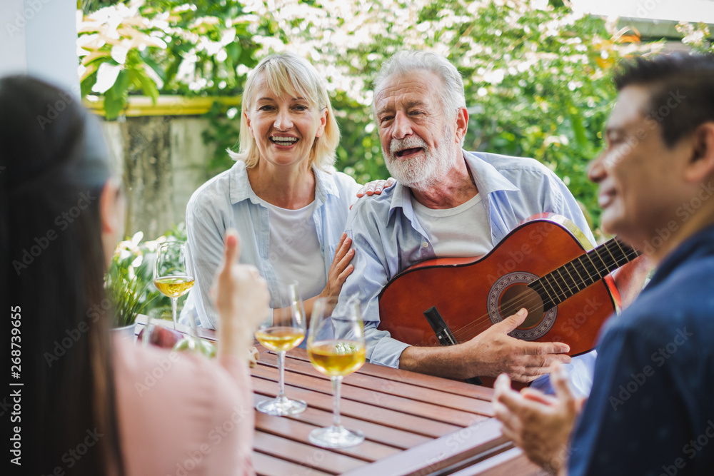 一群老年人在家享受聚会，喝白葡萄酒，唱歌放松