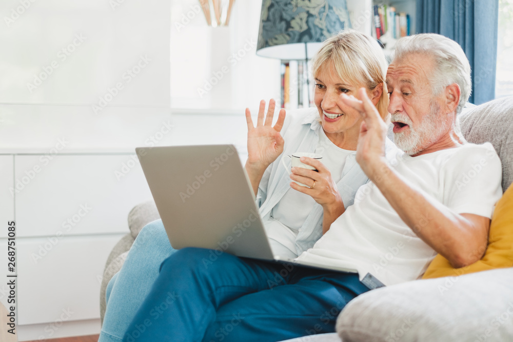 一对老年夫妇在家里的沙发上用电脑笔记本电脑上网购物