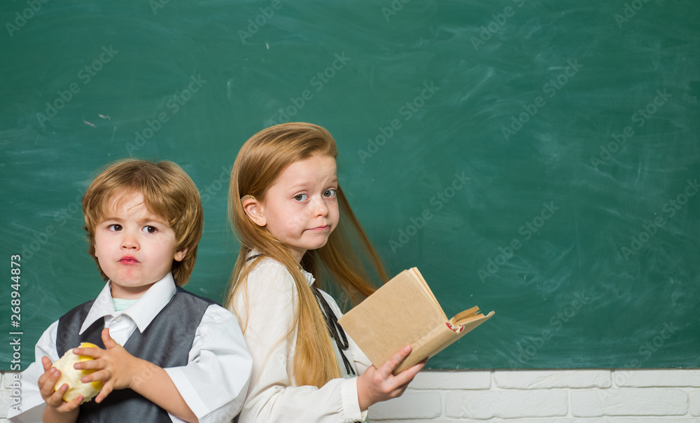 有趣的小男孩和可爱的小女孩指着黑板。复制空格。黑板背景。