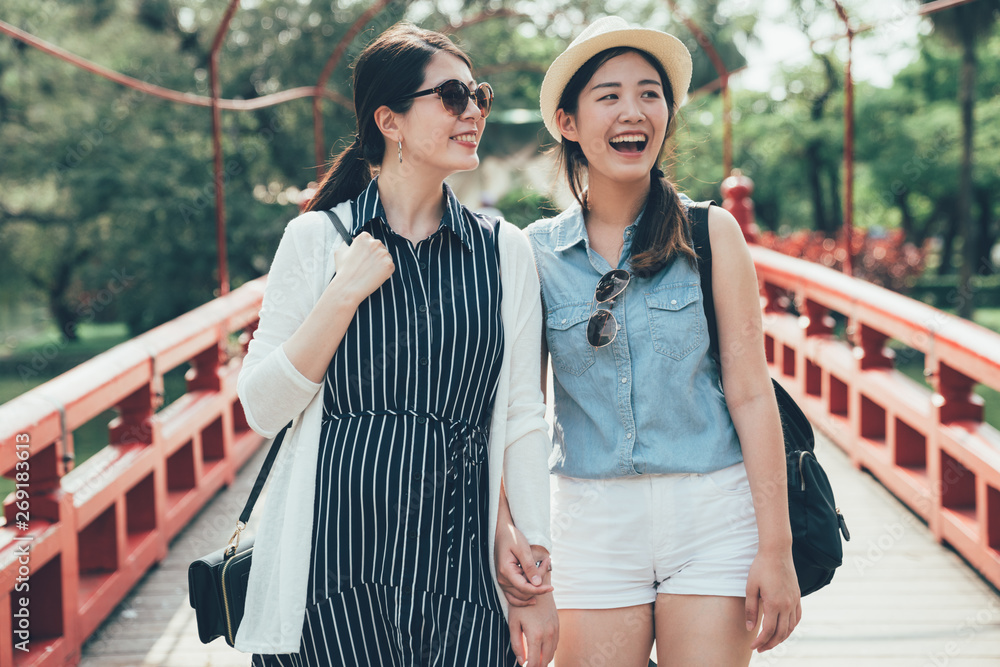 two asian girl friends on walking on beautiful wooden bridge in japanese traditional park. red small