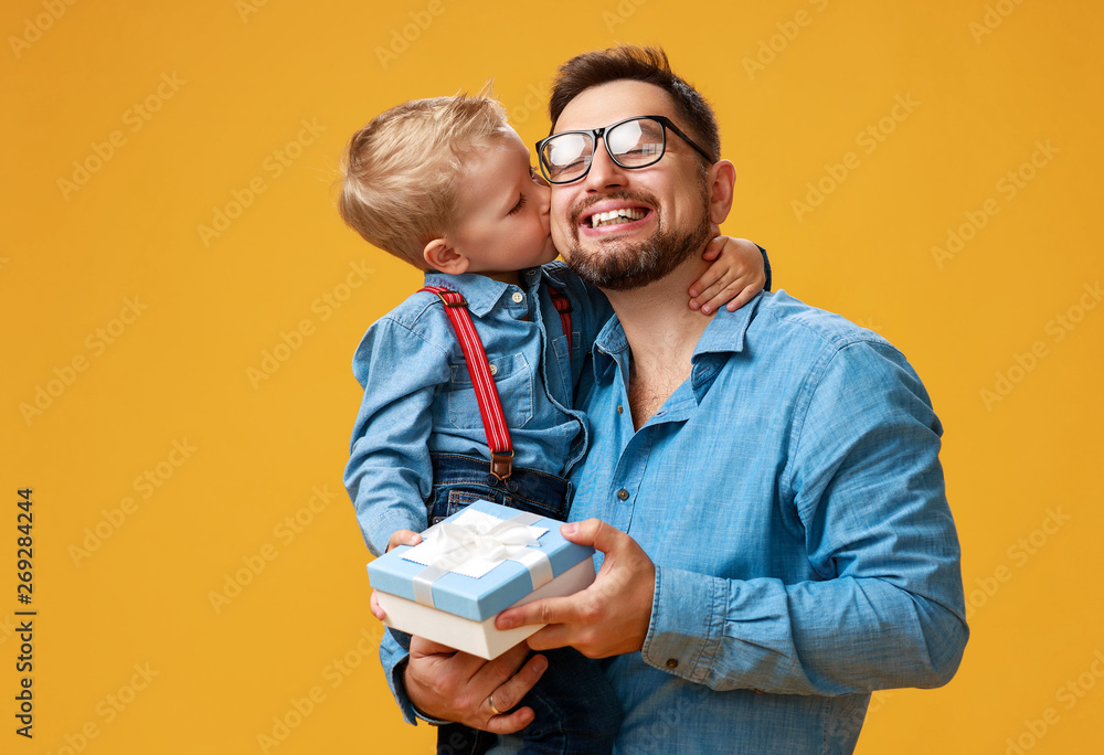 父亲节快乐！可爱的爸爸和儿子在黄色背景下拥抱