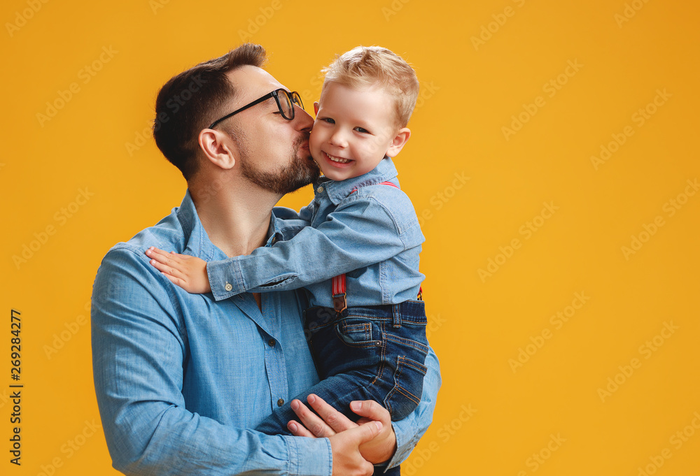 父亲节快乐！可爱的爸爸和儿子在黄色背景下拥抱