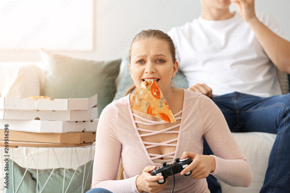 漂亮女人在家玩电子游戏时吃着美味的披萨