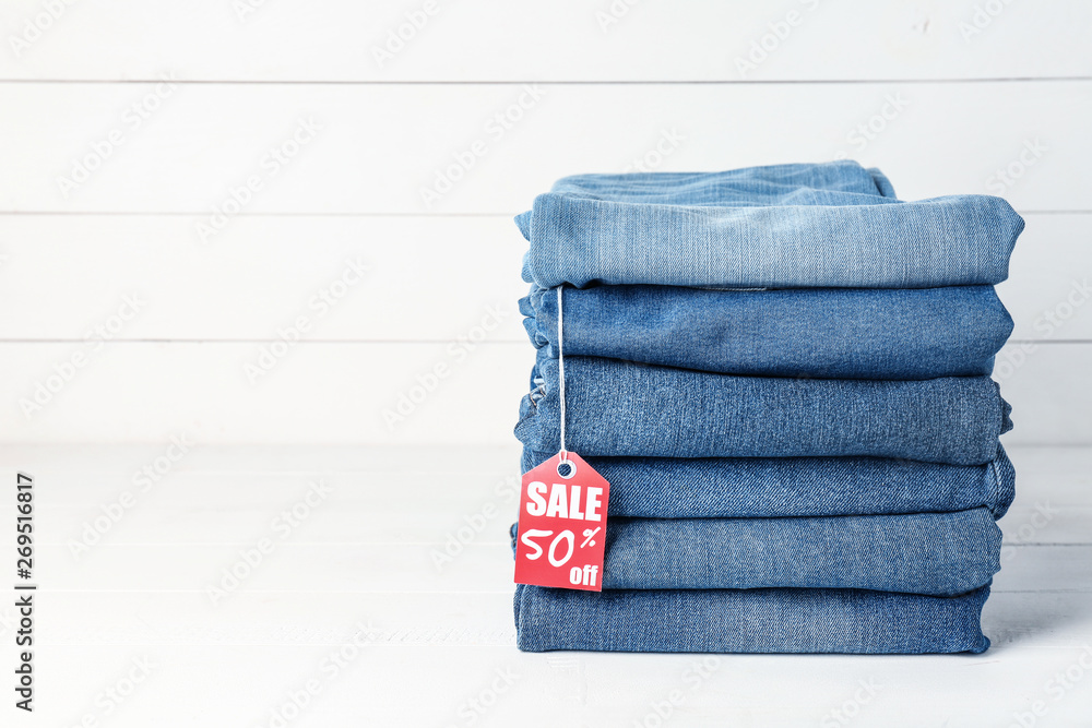 Stack of different jeans pants with shopping tag on white wooden background