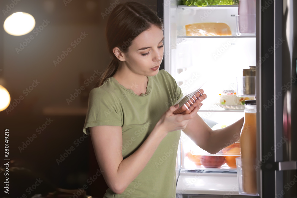 美丽的年轻女子晚上在冰箱里挑选食物
