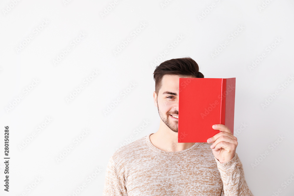 Handsome young man with book on light background
