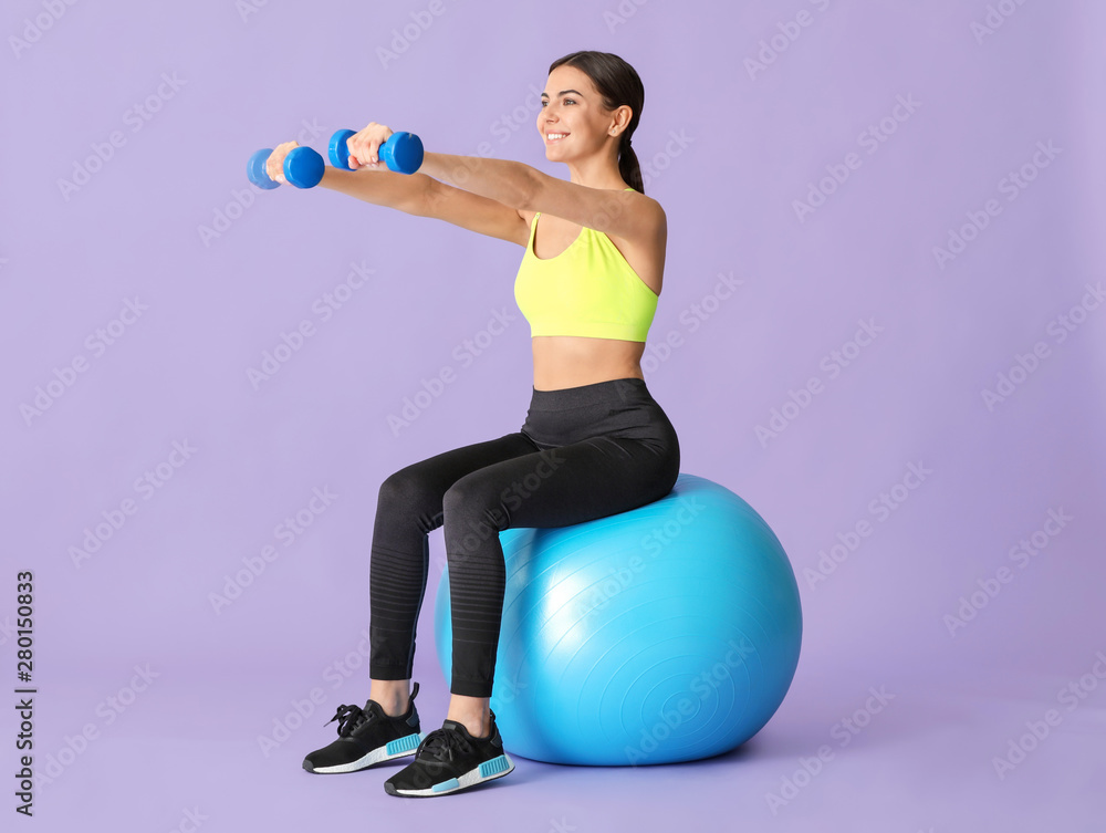 年轻的运动型女性在彩色背景下用健身球进行锻炼